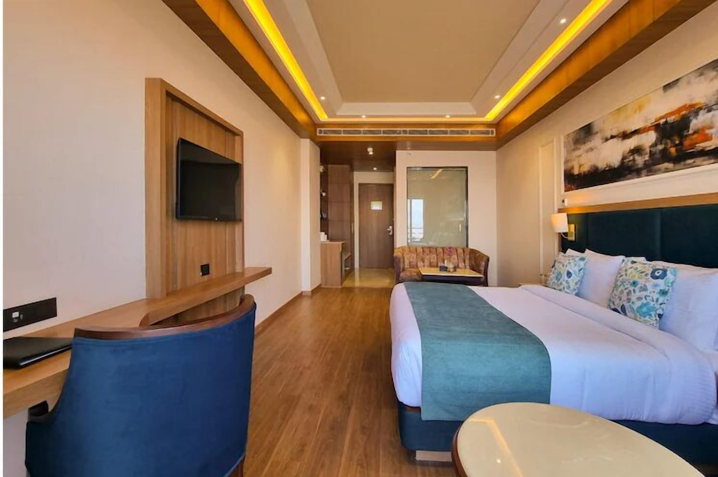 Une chambre d’hôtel moderne équipée d’un lit, d’un bureau, d’une télévision et ornée d’un tableau au mur.