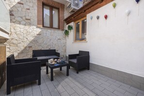 Eine Terrasse im Freien mit Korbmöbeln, einer Steinmauer und einem Fenster mit Fensterläden.