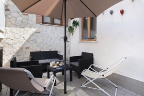 Un patio con mobiliario de mimbre, una mesa con objetos y una planta colgante.