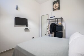 Ein Hotelzimmer mit einem Bett, einem an der Wand befestigten Fernseher, einem Kleiderschrank und einem Spiegel.