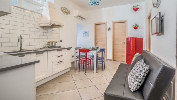 A compact kitchen with white cabinets, a dining area with a red table and chairs, a black leather sofa, and a chandelier. - Two Bedrooms Apt in Sorrento Center with Terrace (Sorrento)