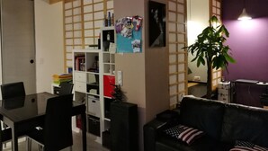 A living room with a dining area, a sofa, a coffee table, a TV, and a bookshelf.