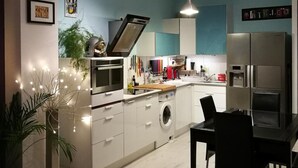 A modern kitchen with white cabinets, a built-in oven, and a stainless steel refrigerator. There is a dining area with a black table and chairs.