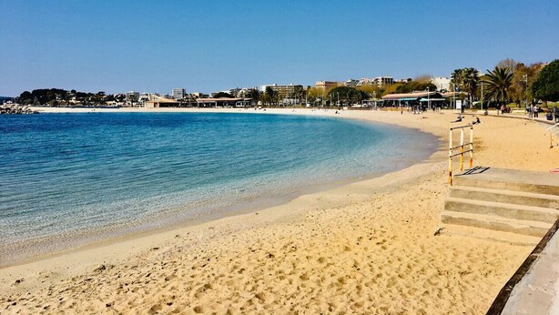 A beach with clear blue water, sandy shore, and a staircase leading down to the water.