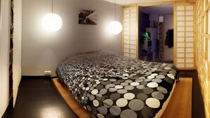 A bedroom with a bed covered in a polka dot blanket, two hanging lights, and a wooden wardrobe with sliding doors.