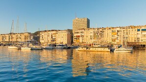 A marina with multiple boats docked, surrounded by multi-story buildings with balconies.