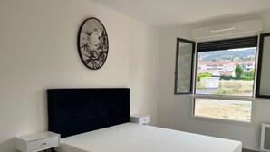 Un dormitorio con cama, mesita de noche, ventana con vistas y una obra de arte colgada en la pared.