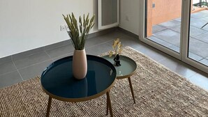 Una sala de estar moderna con un televisor de pantalla plana montado en la pared, una planta en maceta, una mesita redonda y un ventanal corredero que da a un espacio exterior.