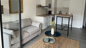 Una sala de estar moderna con un sofá gris, una mesa de centro con un florero, y una zona de cocina con armarios blancos y una mesa de comedor.