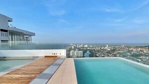 Ein Pool mit unendlicher Weite auf einem Dach, mit Holzterrasse und Blick auf die Stadt.