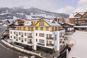 A multi-story hotel with balconies, a sign for 'ALPS KITCHEN', and a snowy mountain backdrop. - Modern apartment with balcony (Fiss)
