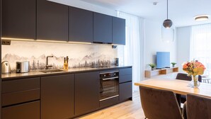 A modern kitchen with dark cabinetry, a built-in oven, and a wooden dining table with chairs. - Modern apartment with balcony (Fiss)