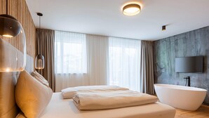 A modern bedroom with a large bed, a freestanding bathtub, and a flat-screen TV mounted on the wall.