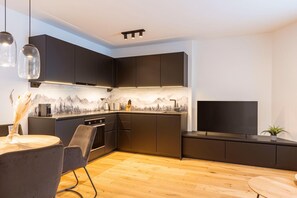 A modern kitchen with dark cabinetry, a wooden floor, and a flat-screen TV mounted above the counter. - Apartment in Fiss with shared sauna (Fiss)