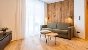 Een moderne woonkamer met een houten accentmuur, een grijze bank, twee ronde houten tafels en een potplant.