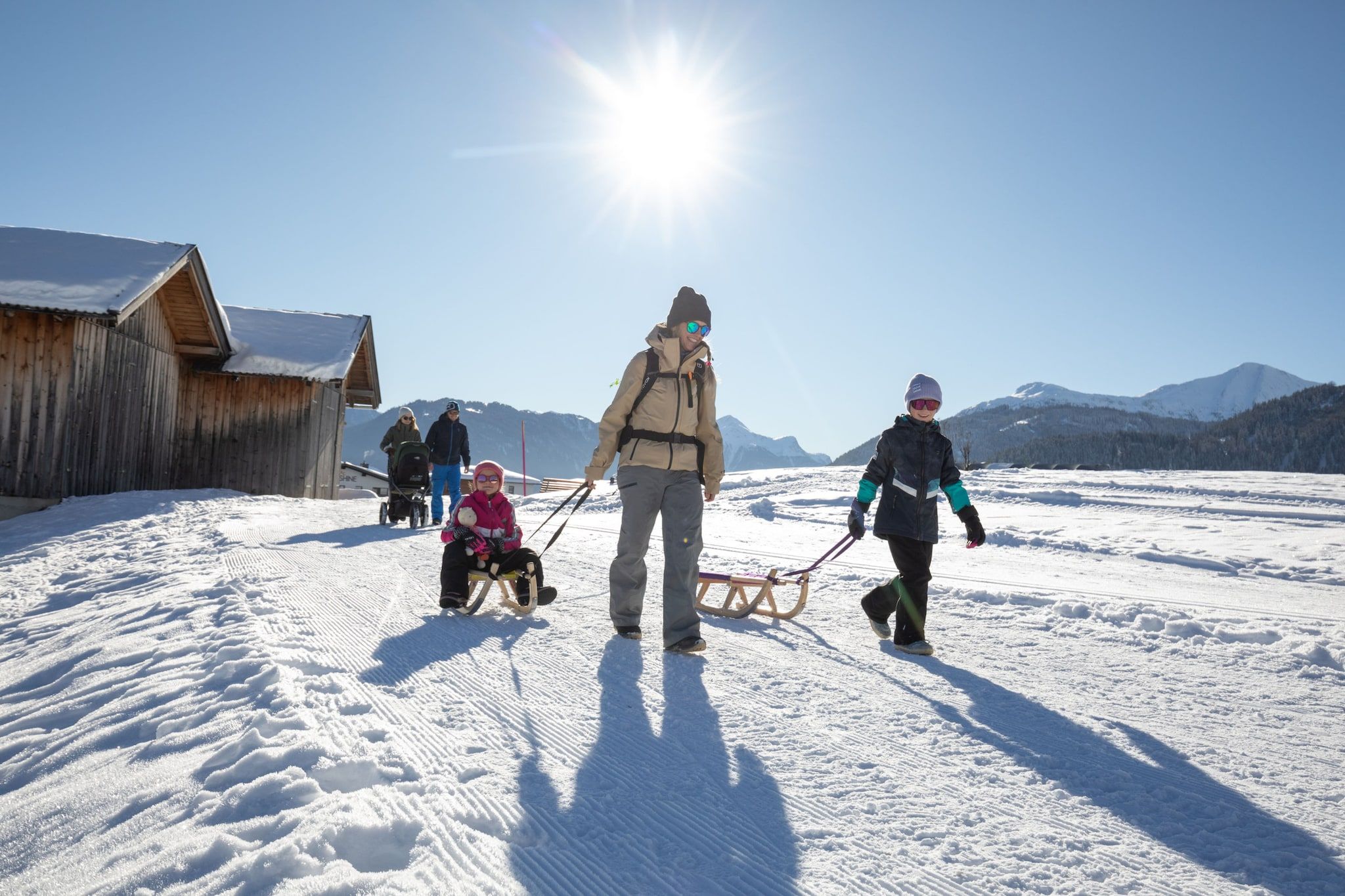 A snowy landscape with a wooden structure, a sled, and people in winter attire.
