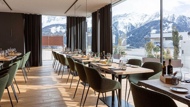 Un'area pranzo con tavoli apparecchiati, ampie finestre che si affacciano su montagne innevate e un design moderno.
