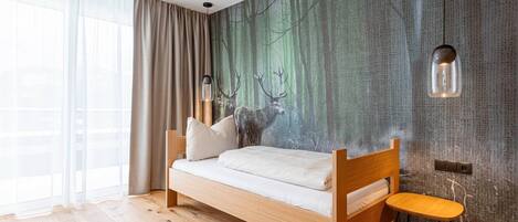 A modern bedroom with a wooden bed, a small stool, and a forest-themed wall mural.