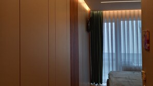 Un dormitorio moderno con una cama grande, un vestidor y vistas al exterior a través de cortinas traslúcidas.