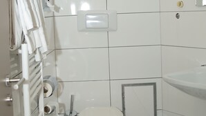 Un baño con azulejos blancos, un inodoro, un lavabo, un perchero para toallas y un cubo de basura.