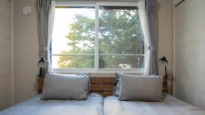 A double bed with two pillows, a window with curtains, and two wall-mounted lamps.