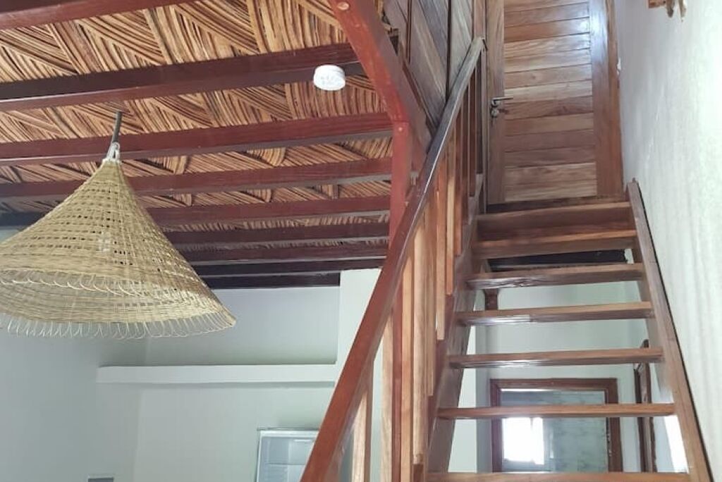 Un escalier en bois surmonté d’un luminaire décoratif au plafond, dont l’abat-jour est fait de fibres tressées.