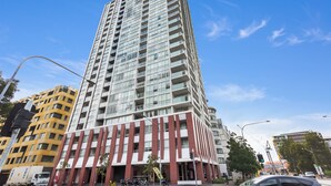 A tall, modern building with a mix of glass and brick facade, multiple balconies, and a prominent entrance with a red brick base. - Bright Zetland Apartment with CBD Views and Fast Free WiFi (Zetland)
