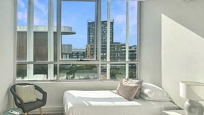 A bedroom with a large window, a bed, a chair, a bedside table, and a lamp. - Bright Zetland Apartment with CBD Views and Fast Free WiFi (Zetland)