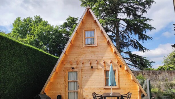 A wooden cabin with a triangular roof, a small porch, and a table with chairs. - Chic, cozy 35m² tepee with swimming pool in Pontacq near Lourdes. (Pontacq)
