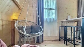 A cozy room with a hanging chair, a cushioned bench, a bar stool, and a window with curtains. - Chic, cozy 35m² tepee with swimming pool in Pontacq near Lourdes. (Pontacq)
