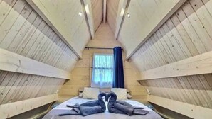 A room with a bed centered under a sloped ceiling, wooden walls, a window with curtains, and a heart-shaped towel arrangement on the bed. - Chic, cozy 35m² tepee with swimming pool in Pontacq near Lourdes. (Pontacq)