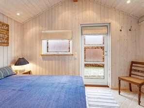 Une chambre confortable avec un lit, une table de chevet, une lampe, un banc en bois et une porte dotée de panneaux en verre dépoli.