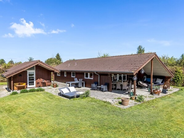 Une maison à deux étages dotée d’un patio, d’un espace extérieur couvert aménagé en coin salon et d’un petit jardin.