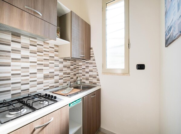 A compact kitchen with a gas stove, a sink, and wooden cabinets.