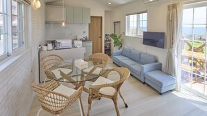 A modern living room with a glass dining table, wicker chairs, a blue sofa, and a TV mounted on the wall. - Solana Shirahama (Minamiboso)