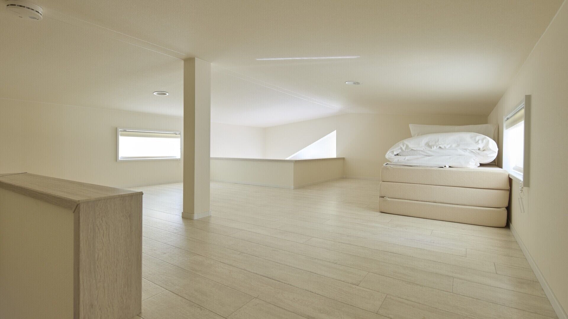 A spacious, modern room with a high ceiling, a built-in bed, and a large window providing natural light.