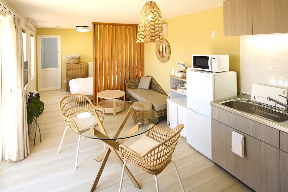 A compact living space with a kitchenette, a dining area with wicker furniture, and a sofa.
