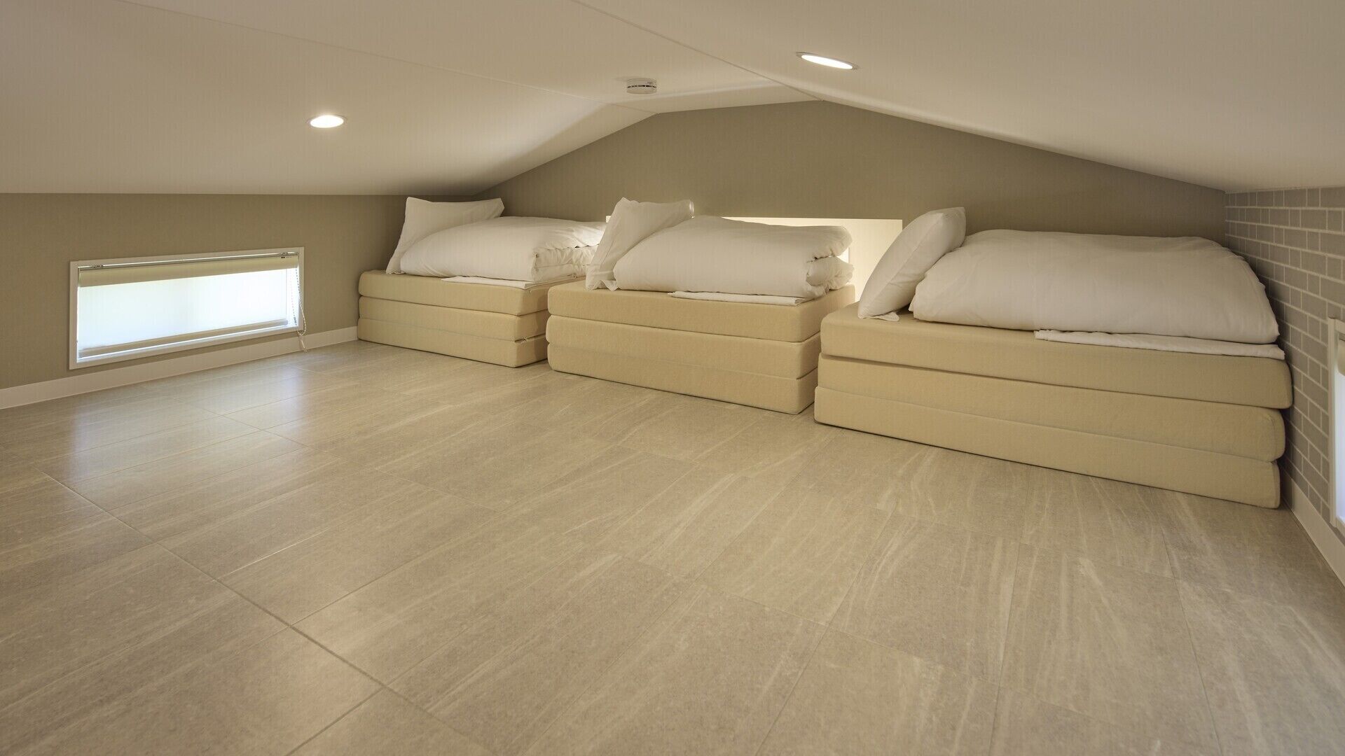 A spacious attic bedroom with a sloped ceiling, built-in benches, and a large window.
