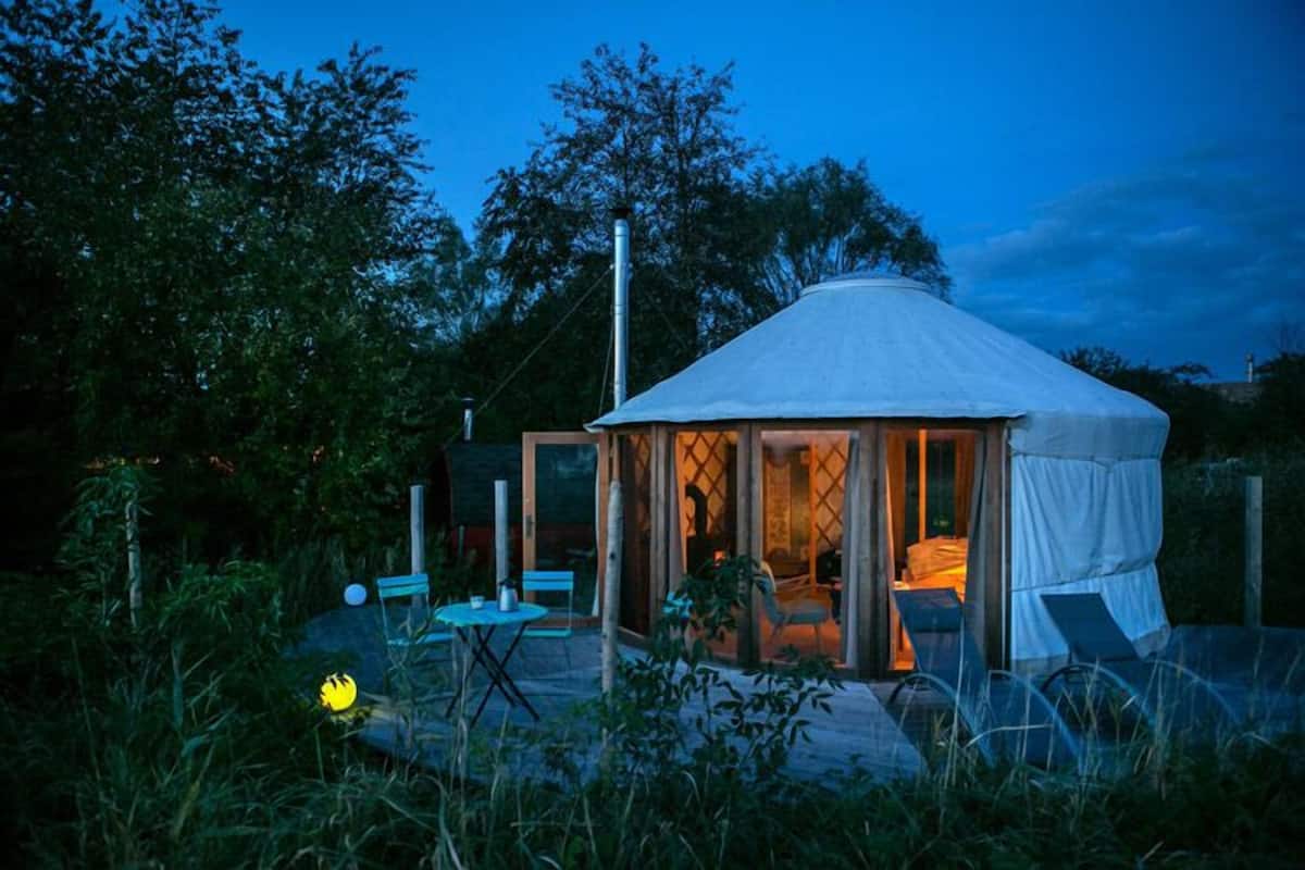 A yurt with a covered entrance, a small outdoor seating area with a table and chairs, and a fire pit.