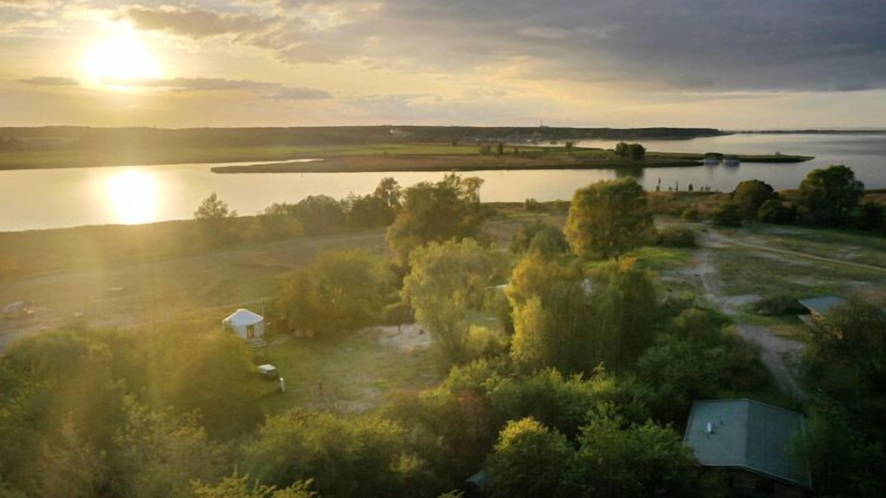 A rural landscape with a body of water, trees, and a small white building.