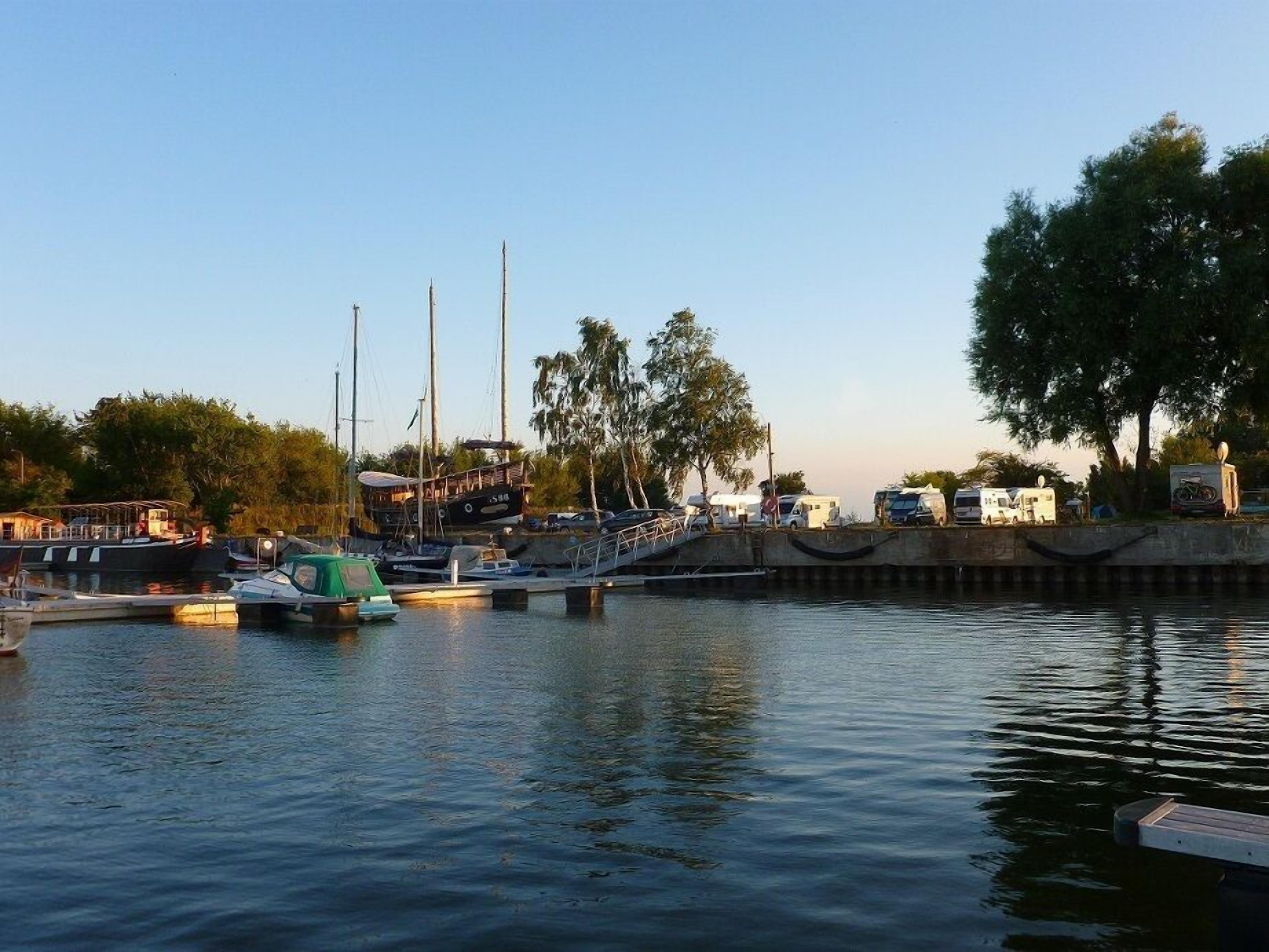 A marina with boats docked, a pedestrian bridge, and RVs parked along the shore.