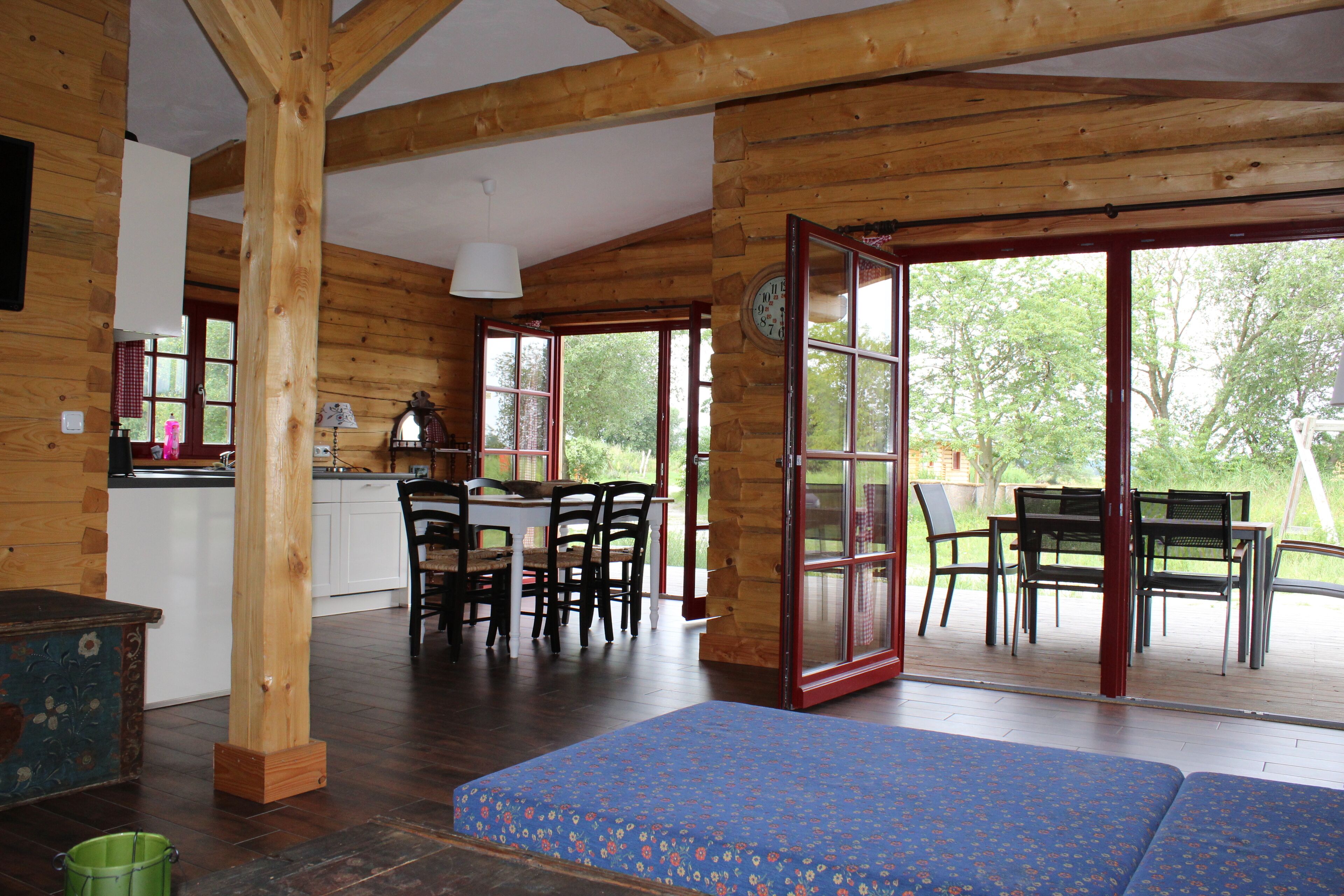Ein Holzblock-Innenraum mit Essbereich, Küche und großen Glasüren, die auf eine Terrassenanlage im Freien führen.