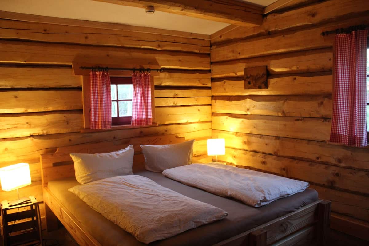 A log cabin room with a double bed, two bedside lamps, and checkered curtains.