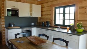 A wooden cabin-style kitchen with white cabinets, a microwave, a coffee maker, and a window with a view. - Halbinsel Peenemünde (Peenemünde)