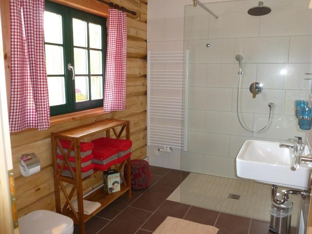 Ein Badezimmer einer Holzhütte mit Dusche, Waschbecken und Fenster mit Karomuster-Vorhängen.