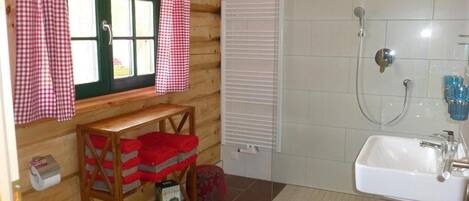 Ein Badezimmer einer Holzhütte mit Dusche, Waschbecken und Fenster mit Karomuster-Vorhängen.
