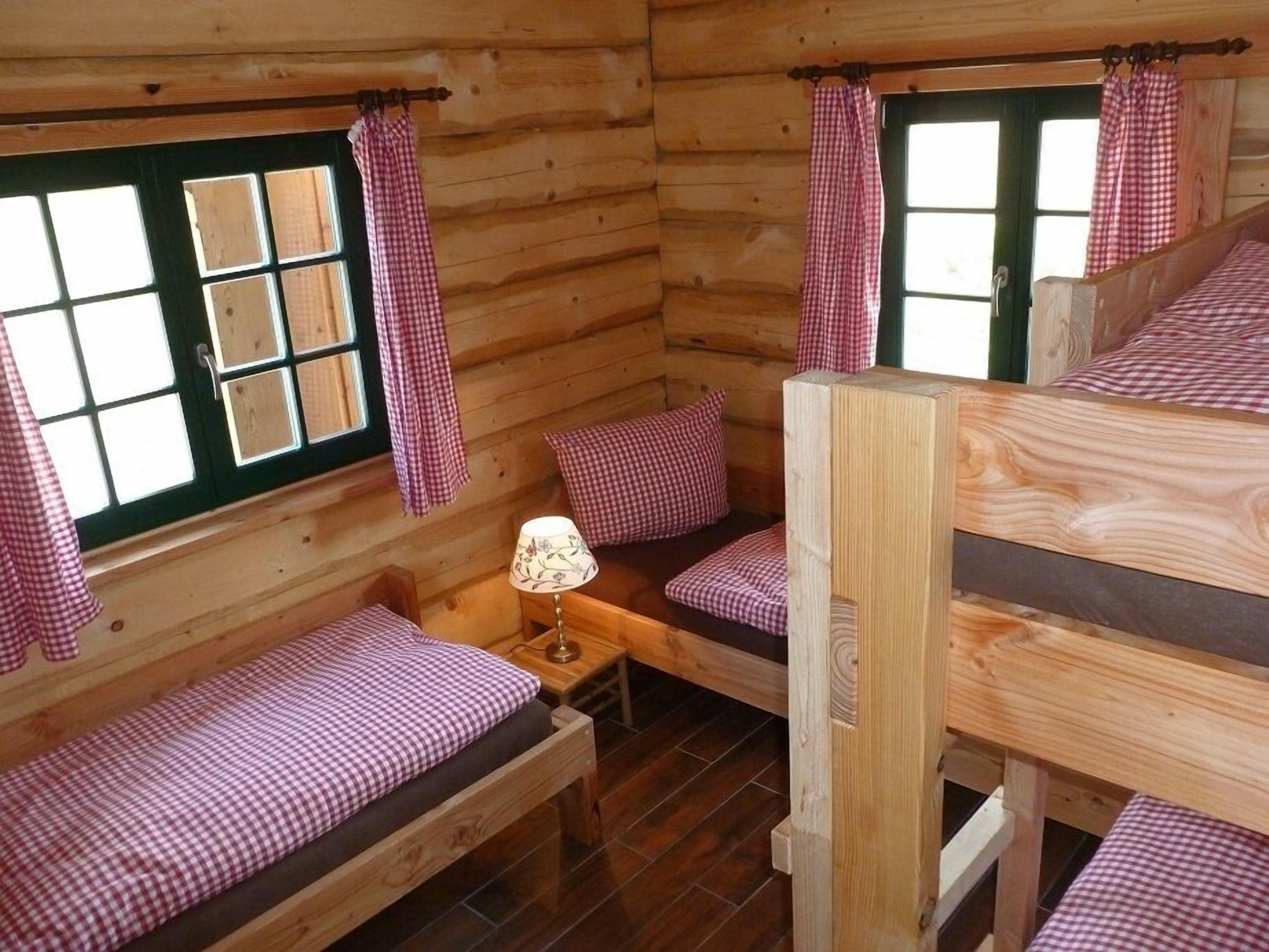 Een blokhut met een slaapzolder, een kleine tafel met een lamp en een raam met geruit gordijnen.