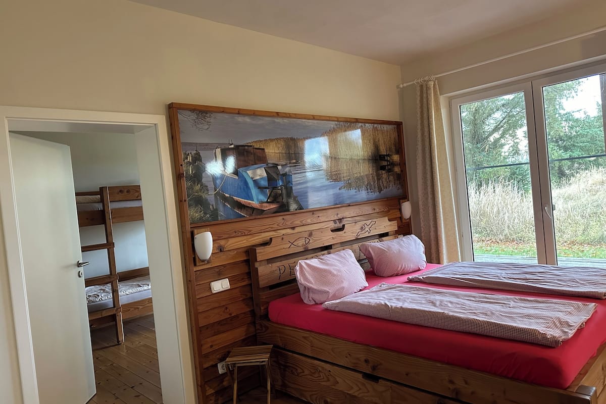 A bedroom with a bunk bed, a wooden headboard, a large mirror, and a window with a view of trees.