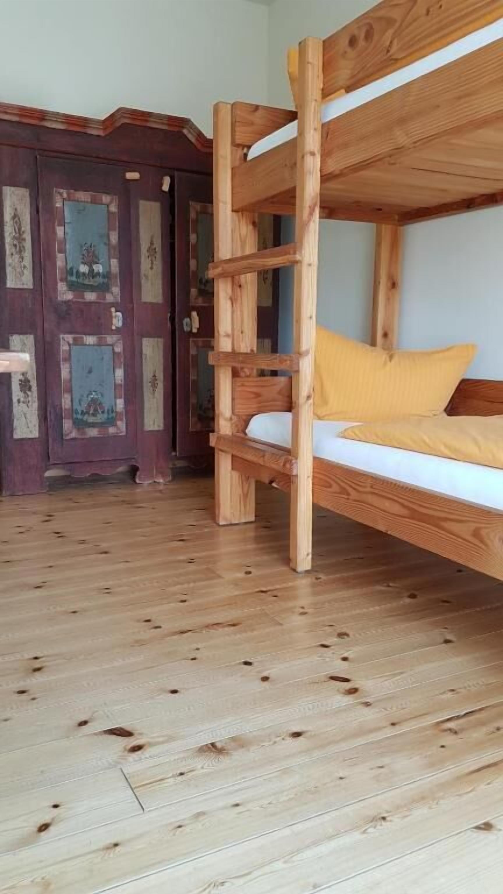Uma cama beliche com escada de madeira, um travesseiro amarelo e piso de madeira.