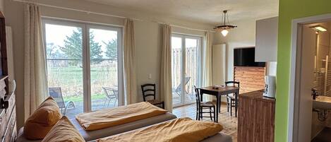 A room with two beds, a wooden desk, and a view of the outdoors.